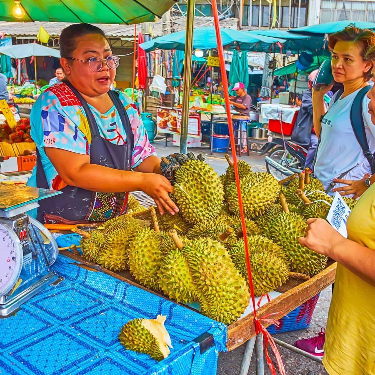 A woman is selling durians at an outdoor market.