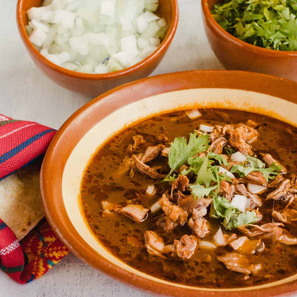 A bowl of mexican soup with meat and tortillas.