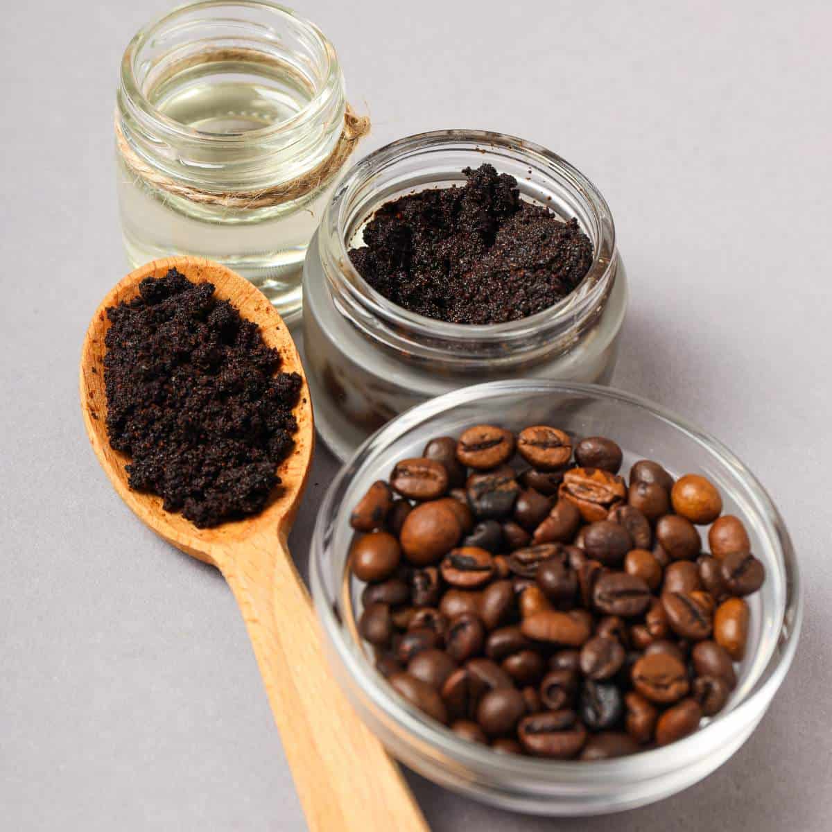 Coffee beans, coffee powder, and a wooden spoon on a gray background.