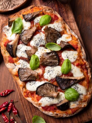 A pinsa with mushrooms and basil on a wooden cutting board.
