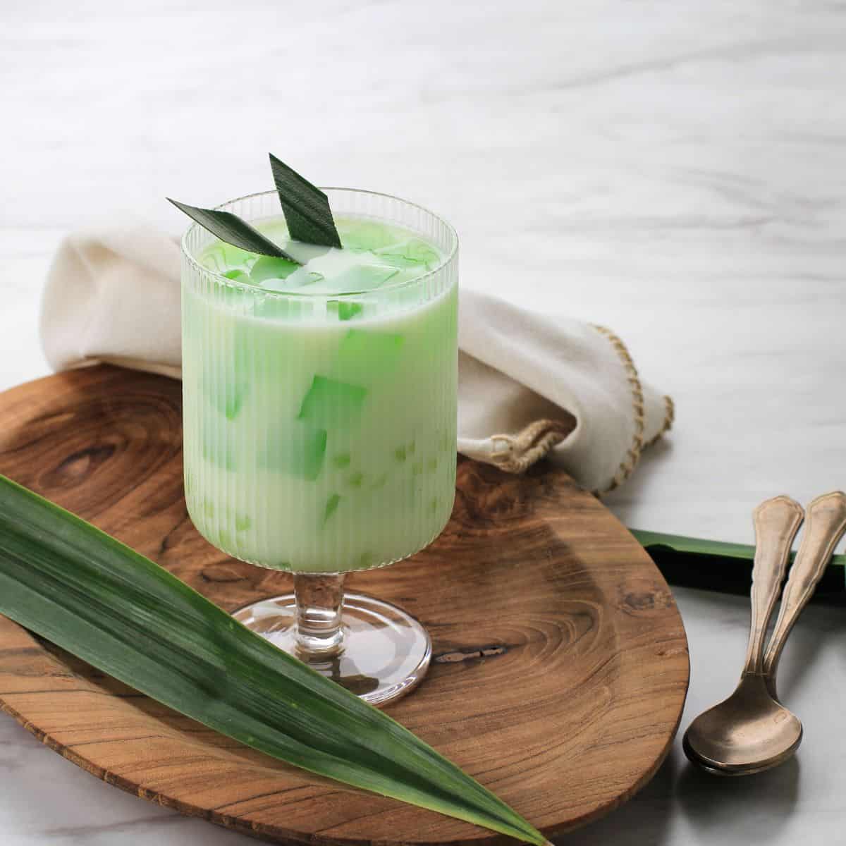 A glass of green tea, a popular Filipino drink, with leaves on a wooden board.