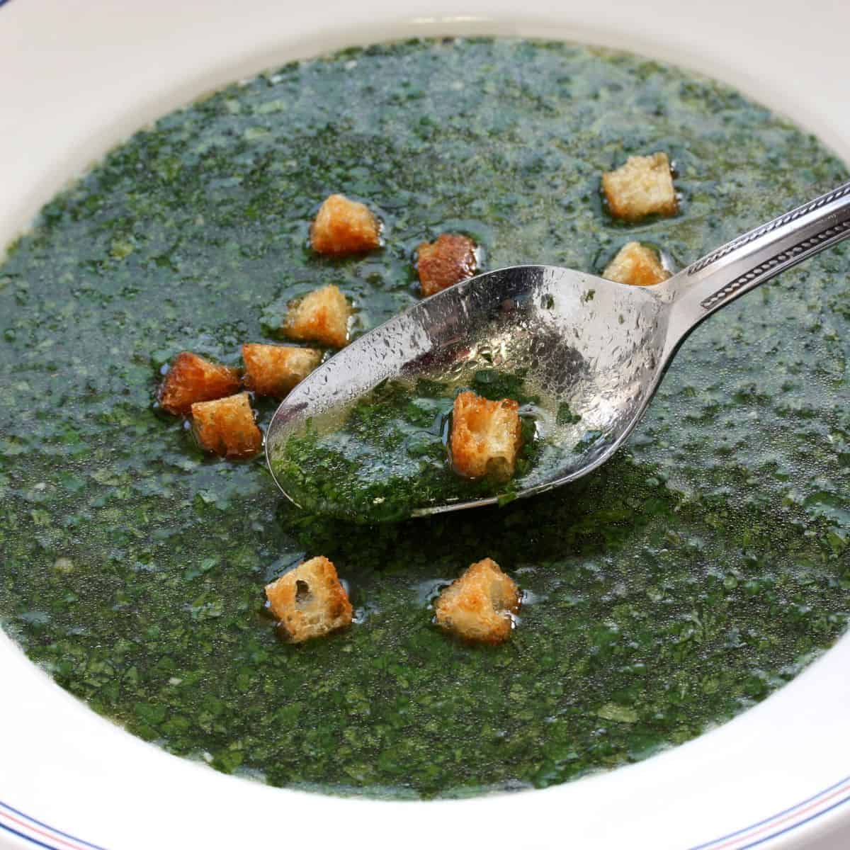A bowl of green soup with croutons in it, a delicious cuisine found in Egypt.