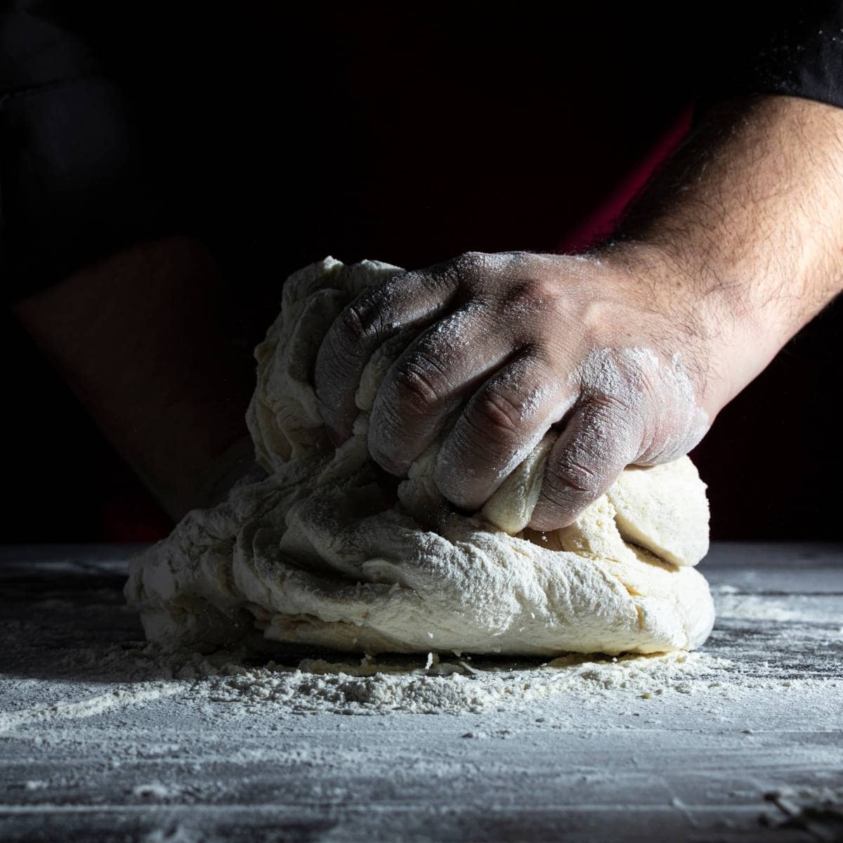 A man is kneading pinsa dough on a table.