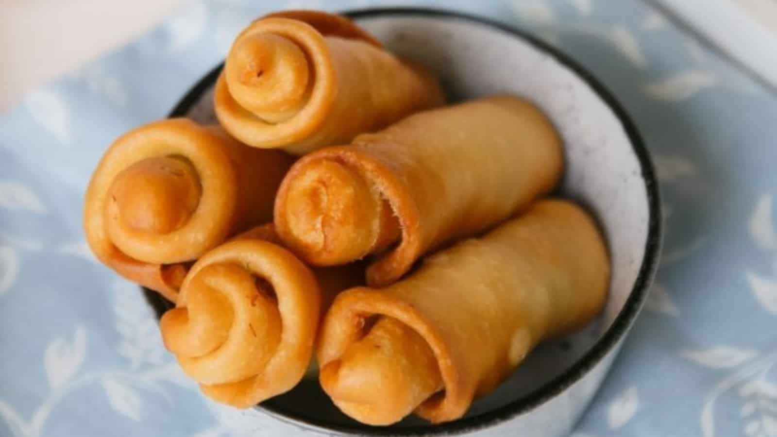A bowl of rolled, golden brown pastries on a blue patterned cloth.