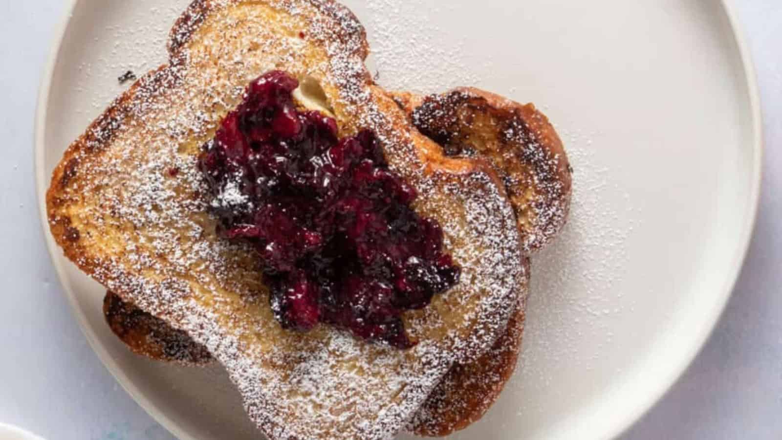 A close-up of French toast topped with berry compote, accompanied by utensils and a cup of coffee.