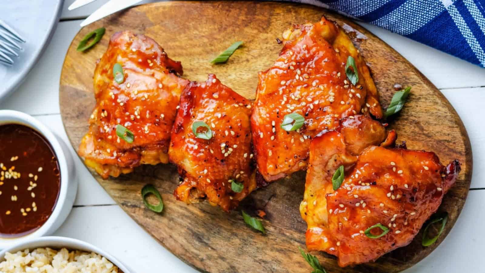 Grilled chicken thighs topped with sesame seeds and green onions on a wooden serving board.
