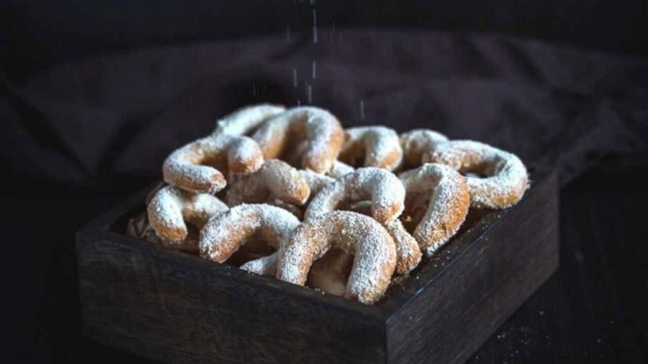 Almond Crescent Cookies on a parchment paper with one piece missing.