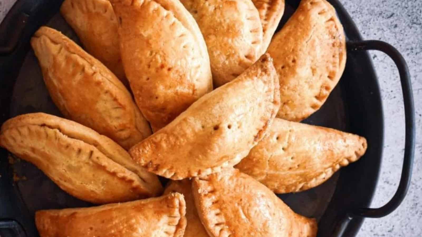 A platter of golden-brown baked empanadas arranged in a circular pattern on a dark dish.