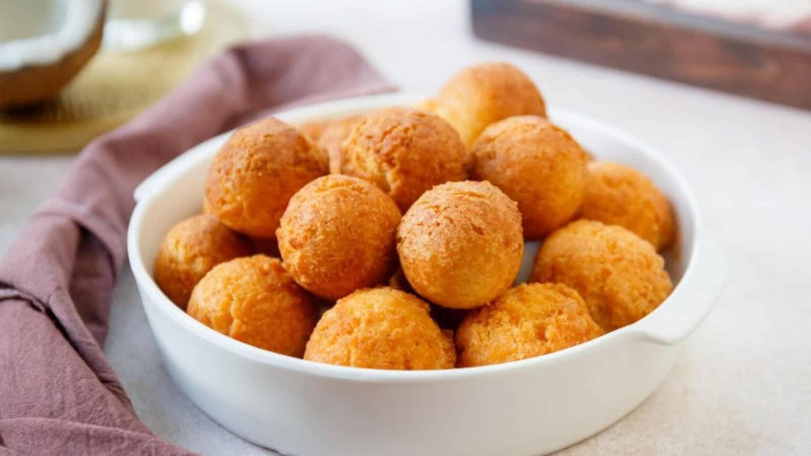 A white dish filled with golden-brown, round fried dough balls on a light surface with a mauve napkin beside it.