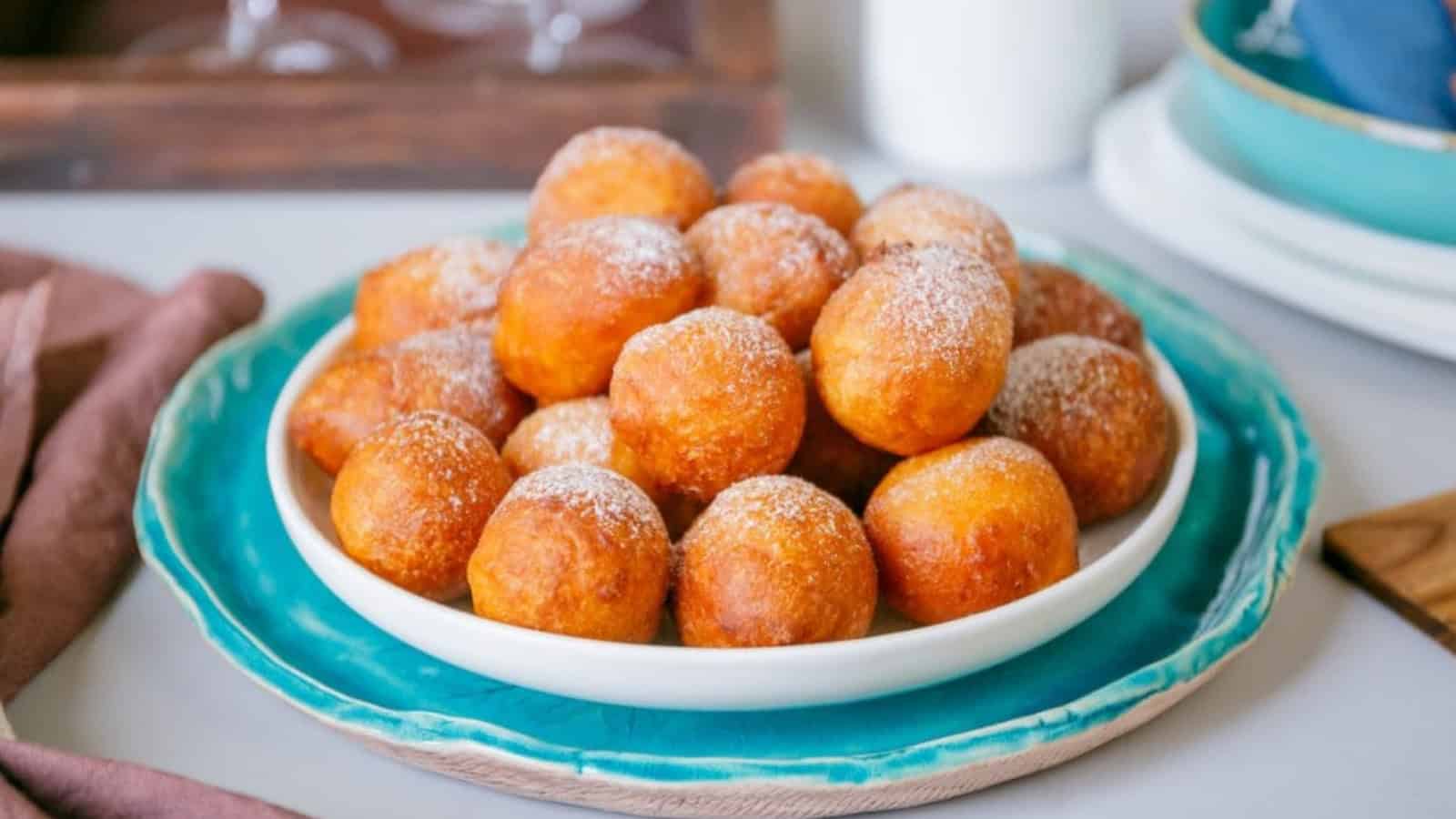 A plate of round, golden-brown fried pastries dusted with powdered sugar.