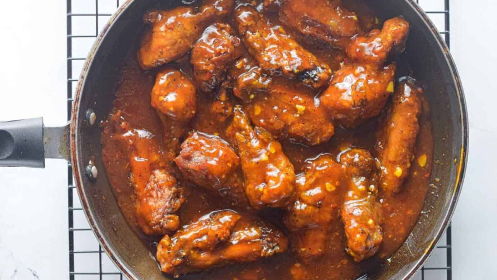 Chicken wings coated in a rich, glossy sauce in a frying pan on a wire rack.