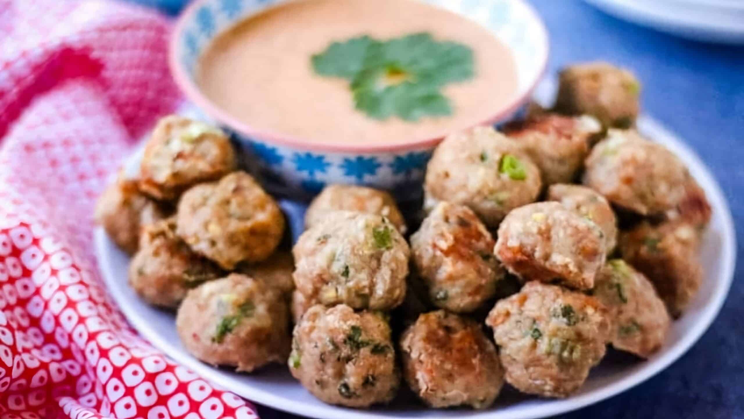 Plate of meatballs next to a bowl of dipping sauce with a parsley garnish.