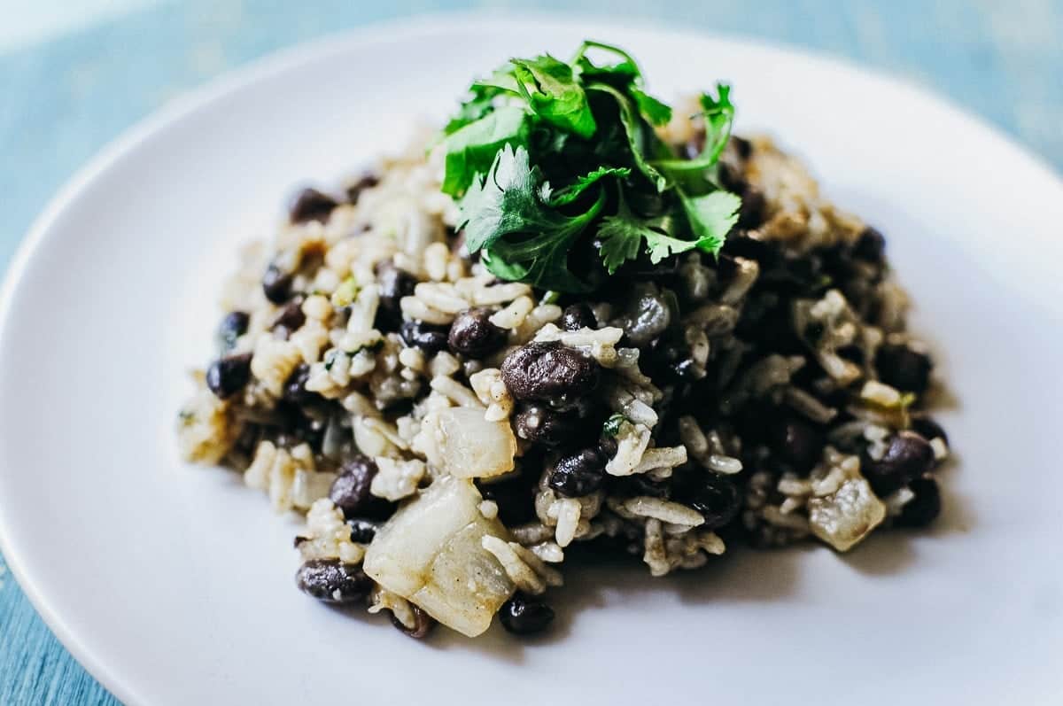 A plate of rice and black beans topped with fresh cilantro on a white surface.