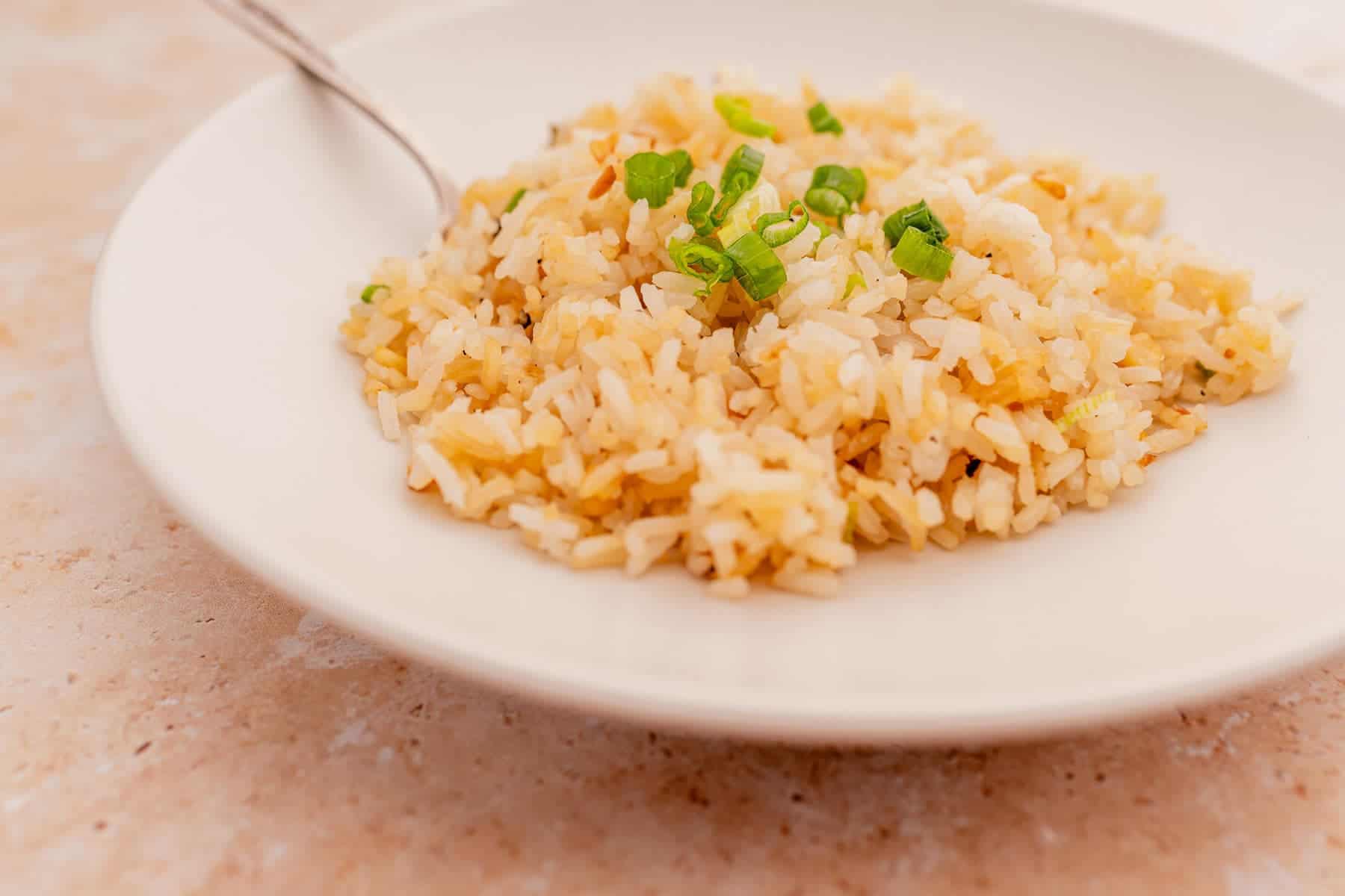 A plate of fried rice garnished with chopped green onions, with a fork on the side.