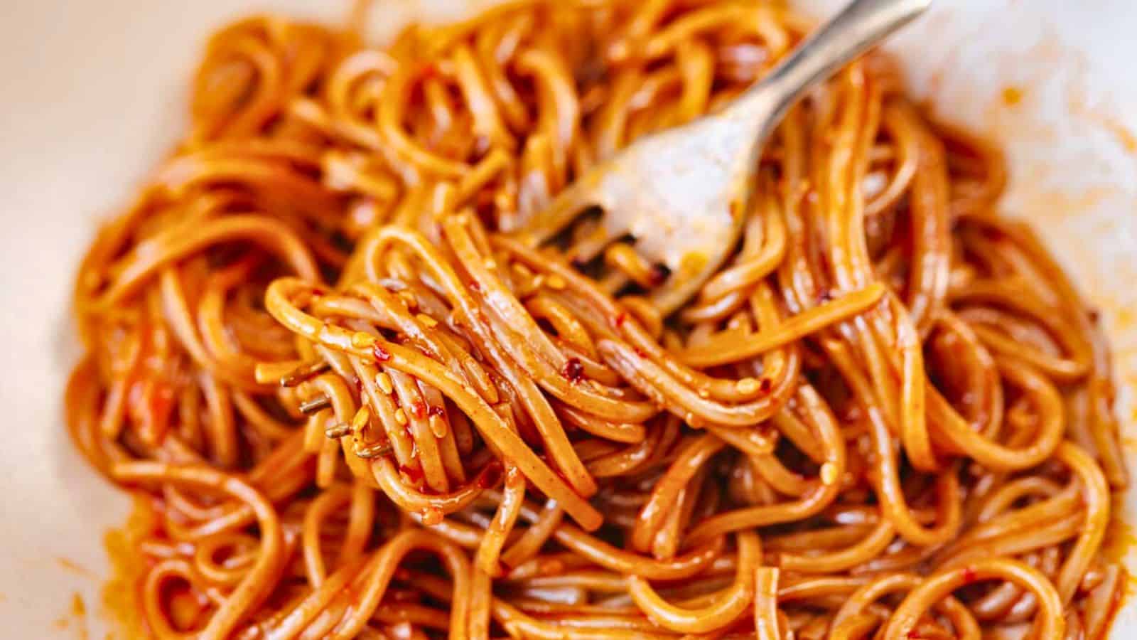 A fork twirls a serving of spaghetti coated in a red sauce with visible chili flakes.
