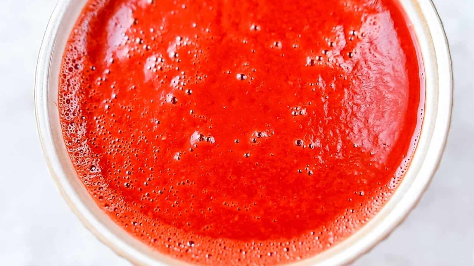 A bowl filled with bright red tomato sauce, showing a smooth texture with small bubbles on the surface.