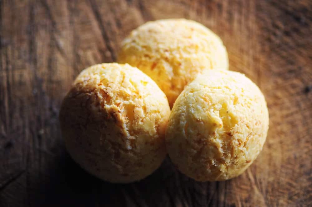 Three round, golden-brown cheese bread rolls on a textured wooden surface.