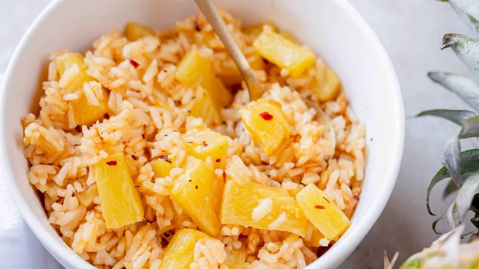 A white bowl filled with rice and pineapple chunks, with a spoon.
