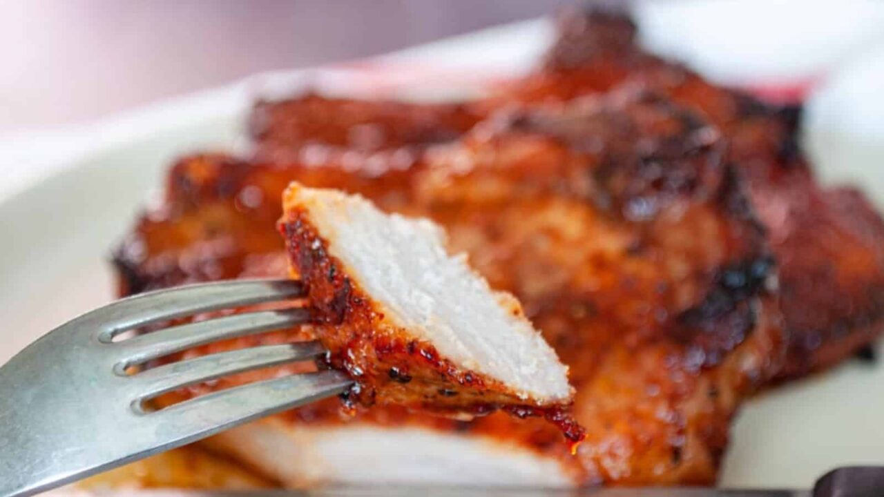 Close-up of a fork holding a piece of grilled meat with a charred exterior, resting on a white plate.
