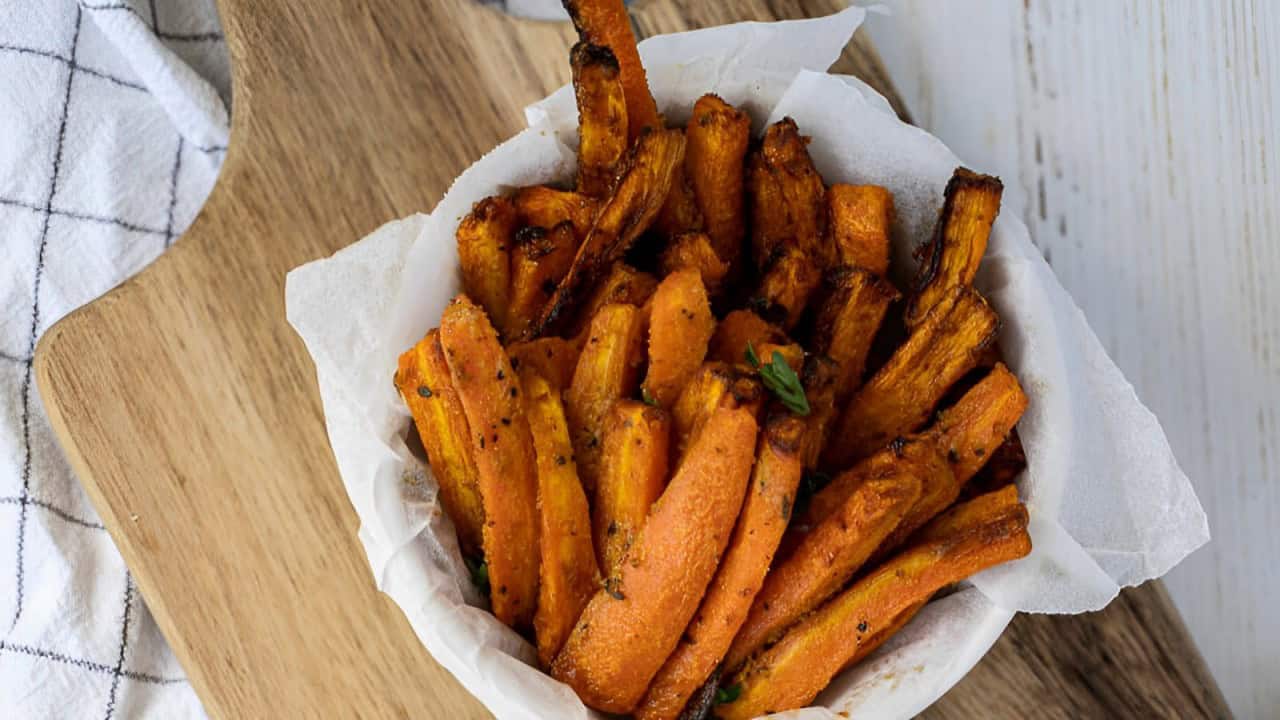 A bowl of seasoned sweet potato fries on a wooden cutting board and white cloth.