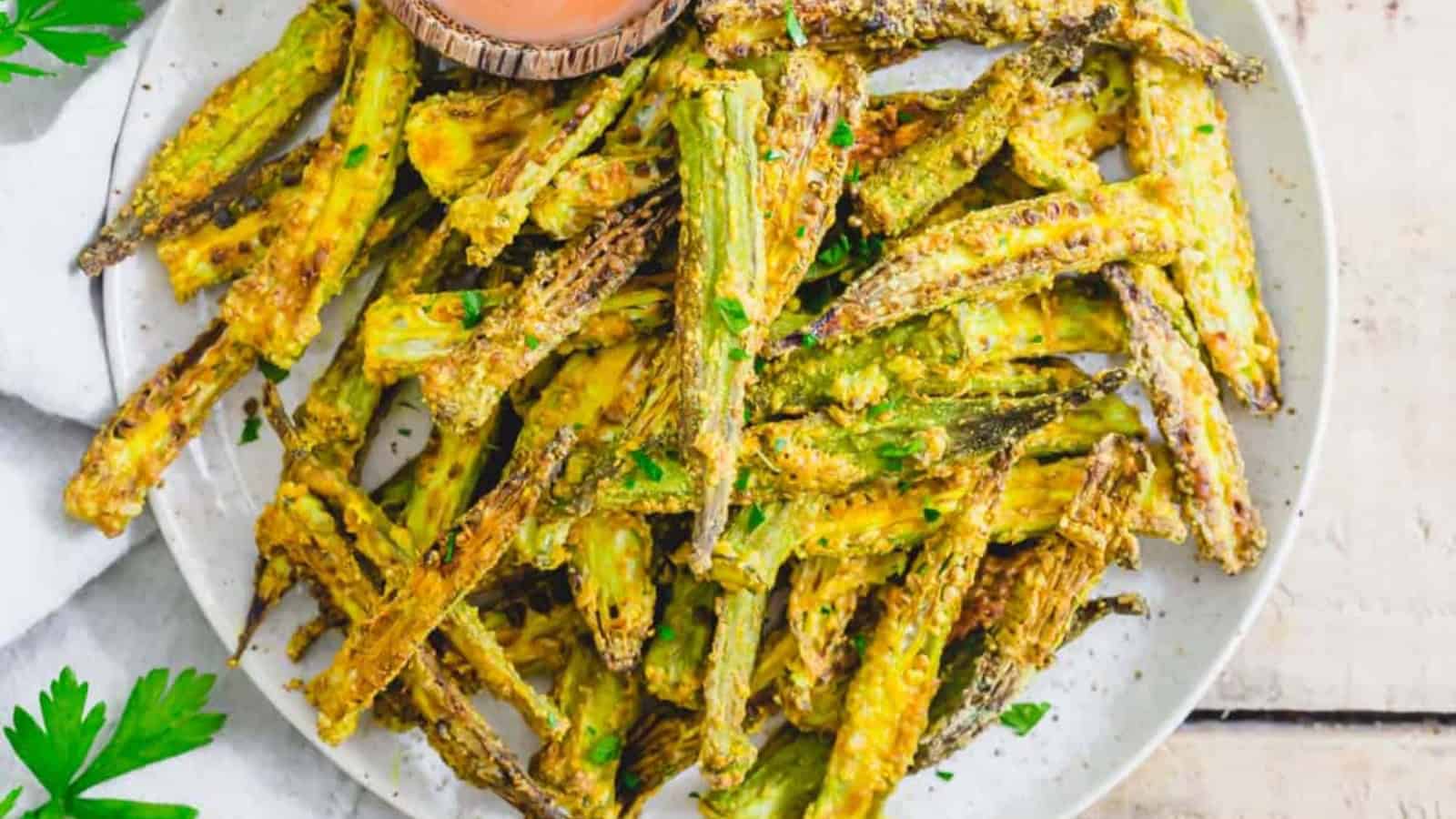 A plate of crispy fried okra garnished with herbs, accompanied by a bowl of dipping sauce.