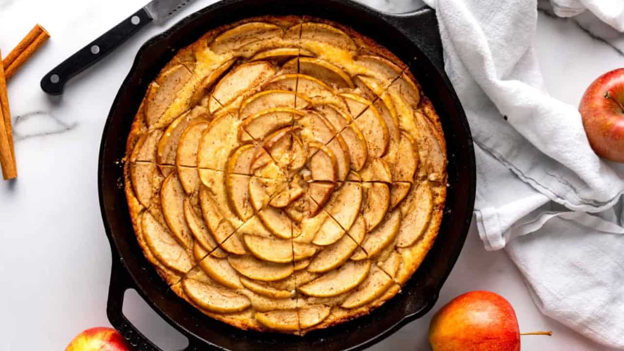 An apple cake baked in a cast iron skillet, cut into slices.