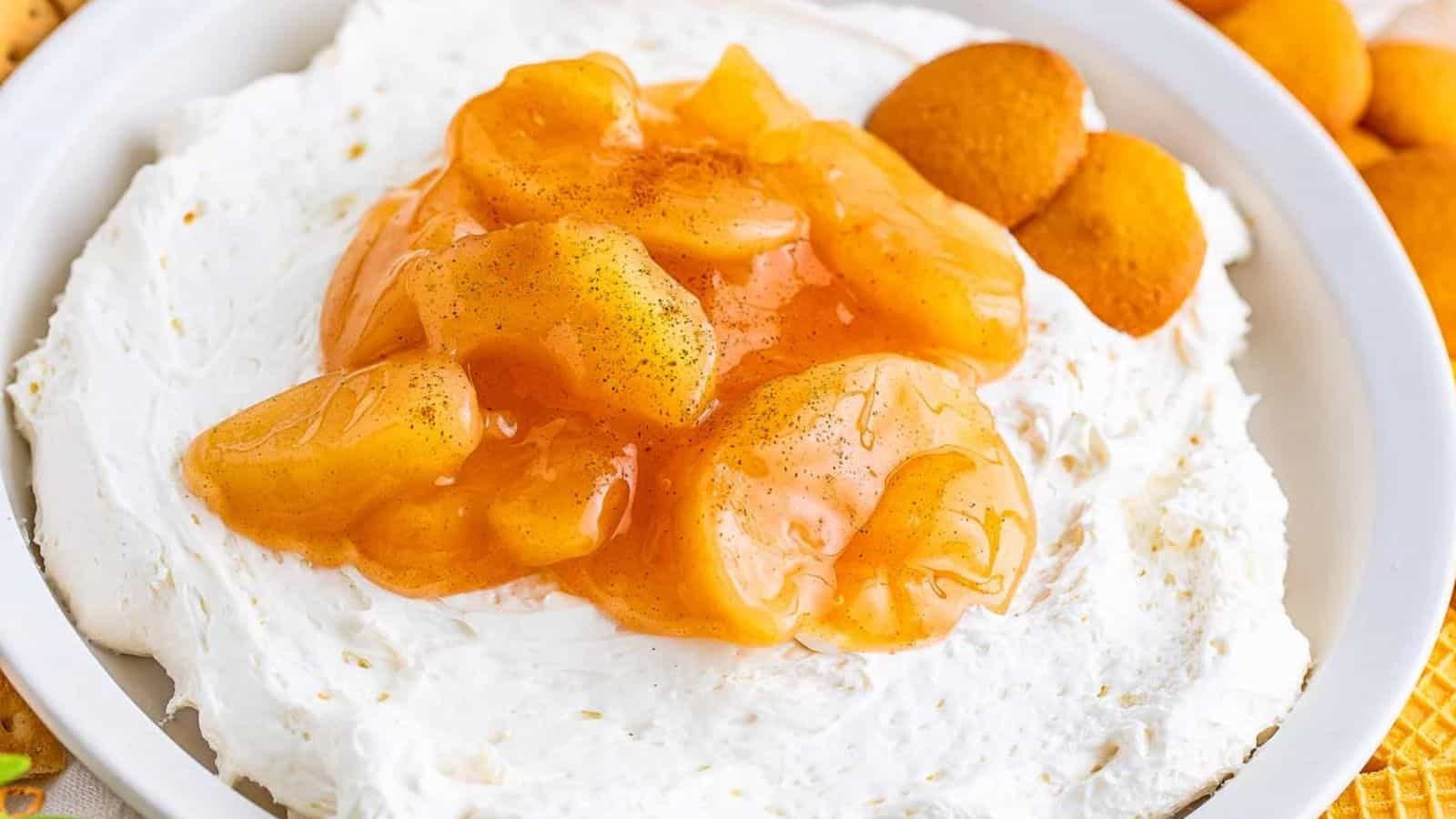 A bowl of creamy dip topped with caramelized apple slices and surrounded by round cookies.
