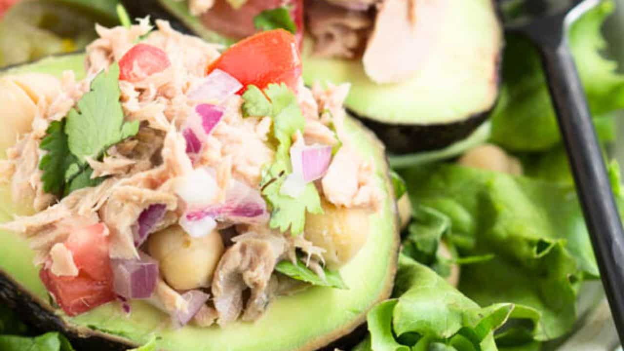 Avocado halves filled with a mixture of tuna, diced tomatoes, red onions, chickpeas, and cilantro, served on a bed of green lettuce.