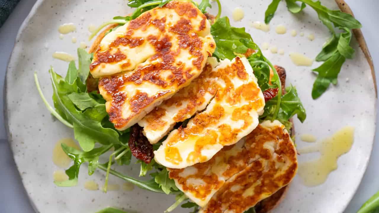 Grilled halloumi slices on a bed of arugula, drizzled with olive oil, served on a plate.