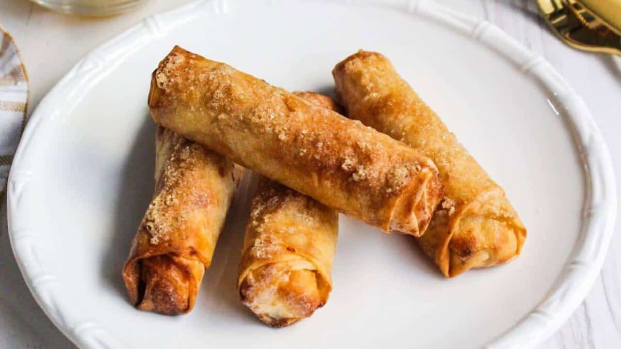 Four crispy fried spring rolls on a white plate.