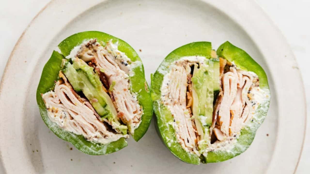 Sliced green bell pepper stuffed with turkey, avocado, mushrooms, and cream cheese on a white plate.