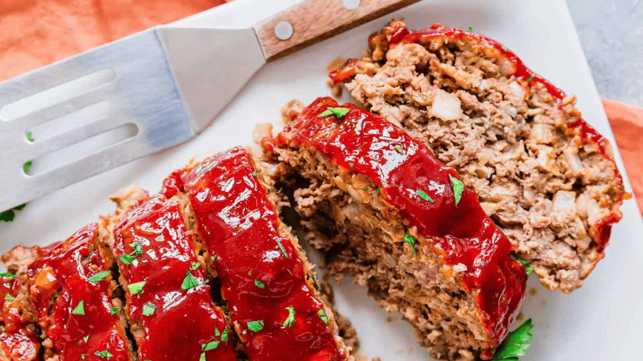 Meatloaf on a white plate cut into slices with fresh parsley garnish.