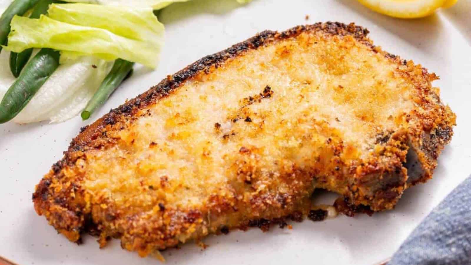 A breaded and baked fish fillet on a plate, garnished with green beans and lettuce.