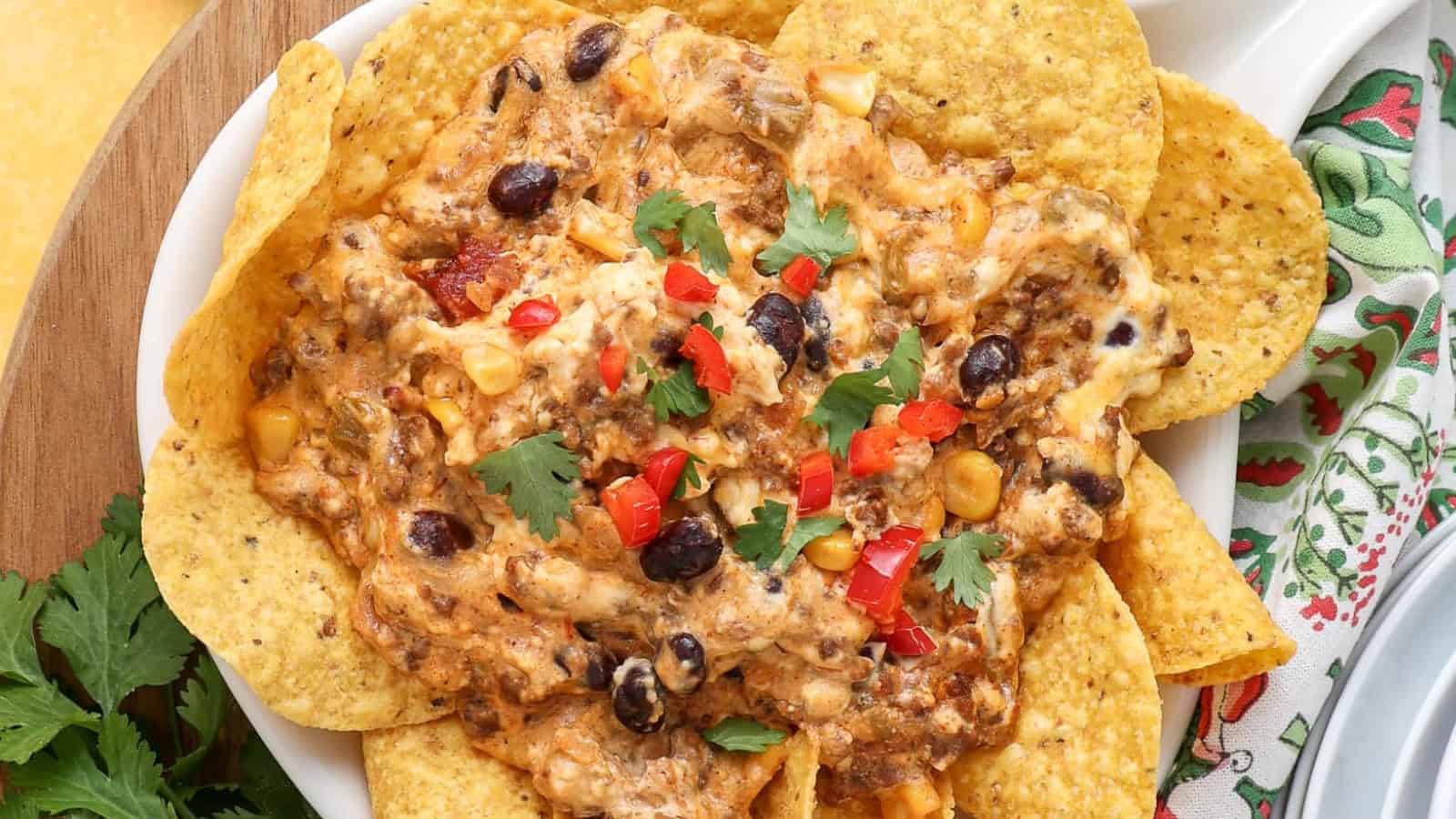 A plate of nachos topped with melted cheese, black beans, corn, diced red peppers, and cilantro.