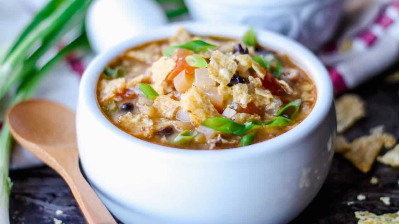 A bowl of hot soup with vegetables and garnished with green onions. A wooden spoon is beside the bowl.