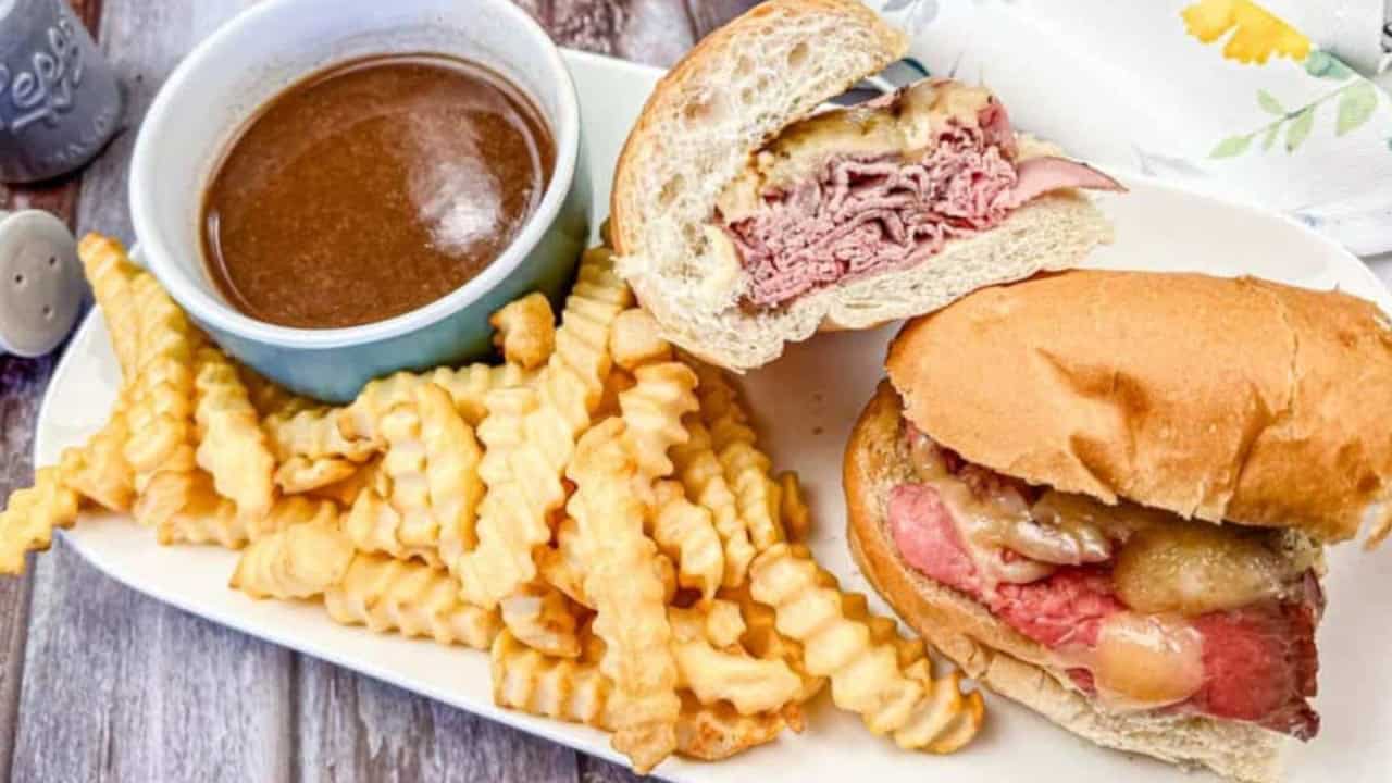 Plate with two roast beef sandwiches, a cup of brown dipping sauce, and crinkle-cut fries.