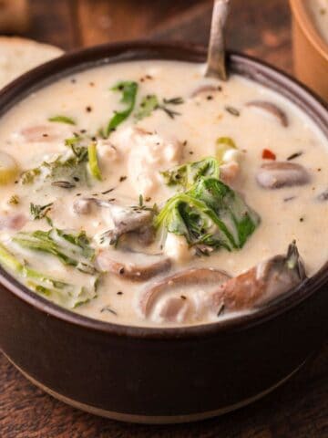 A bowl of creamy mushroom soup garnished with herbs and greens, with slices of bread on the side.