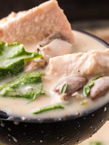 Ladle scooping creamy soup with chicken pieces, mushrooms, and greens.