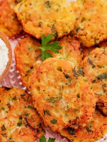 A plate of crispy fritters garnished with fresh parsley, accompanied by a small dish of creamy dip topped with parsley.