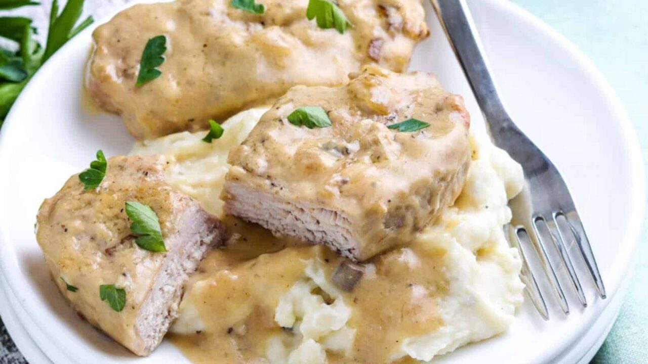 Plate with sliced turkey breast in creamy sauce on mashed potatoes, garnished with parsley, and accompanied by a fork.