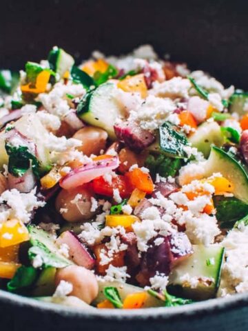 A bowl of mixed salad with chickpeas, diced cucumbers, tomatoes, red onions, parsley, and crumbled feta cheese.