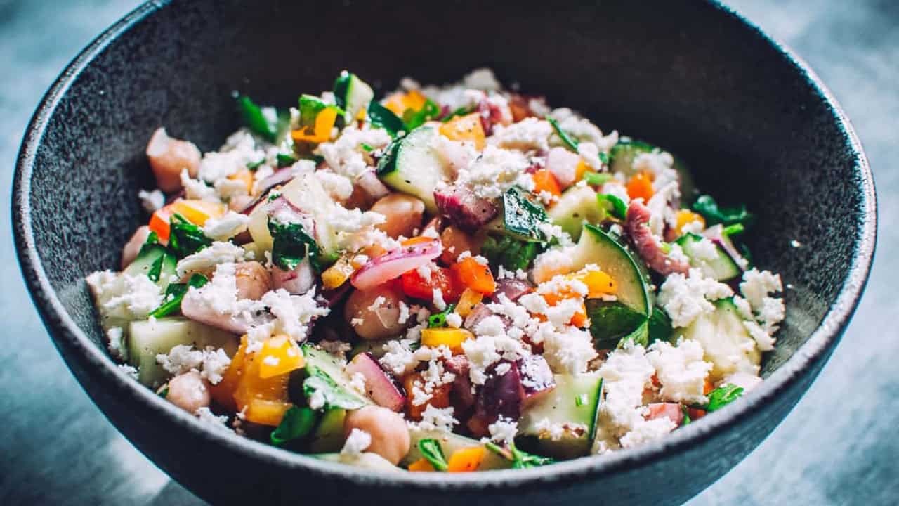 A bowl of mixed salad with chickpeas, diced cucumbers, tomatoes, red onions, parsley, and crumbled feta cheese.