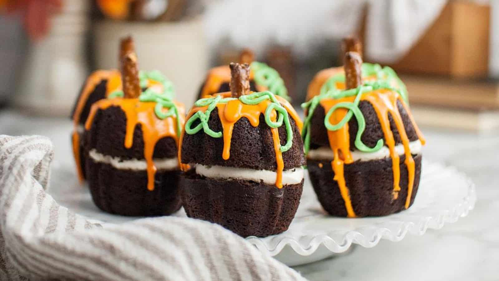 Chocolate cakes shaped like pumpkins with orange and green icing and pretzel stems on a white plate.