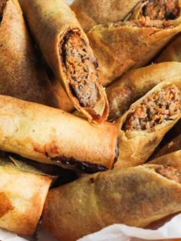 A plate of crispy spring rolls filled with a vegetable and meat mixture, cut in halves to show the filling.