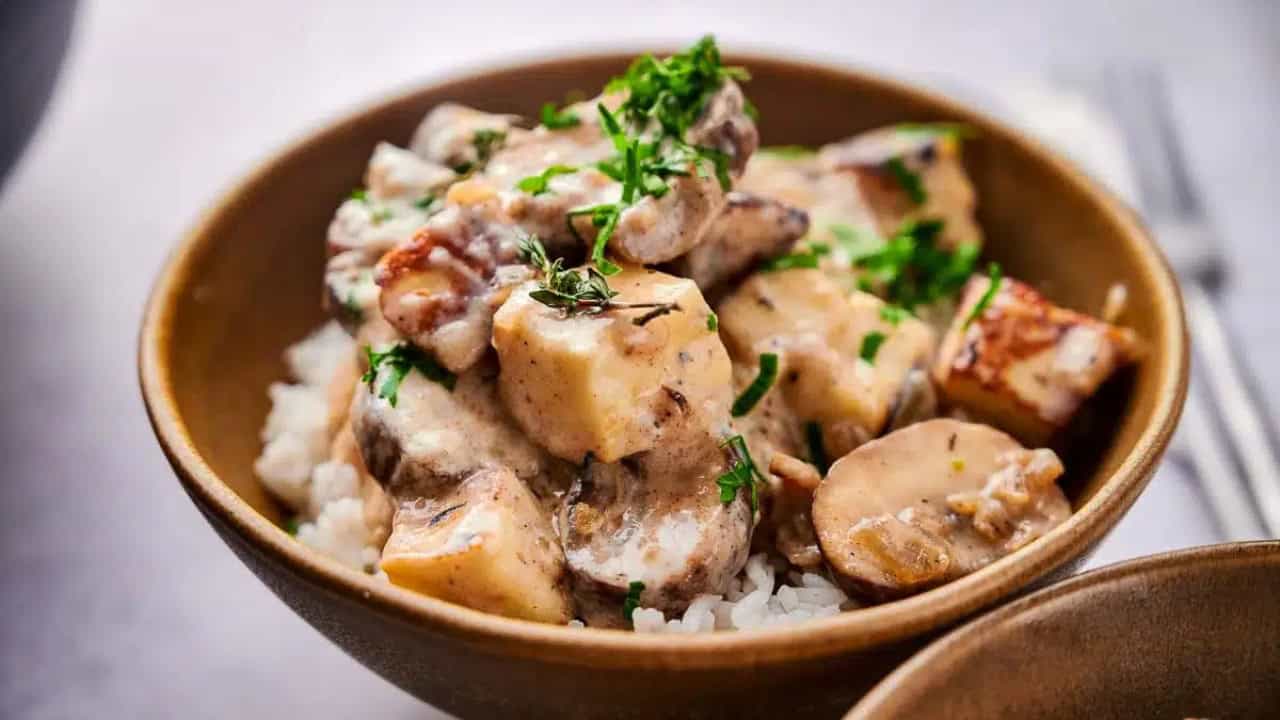 A bowl of rice topped with creamy mushroom stew, garnished with fresh herbs.