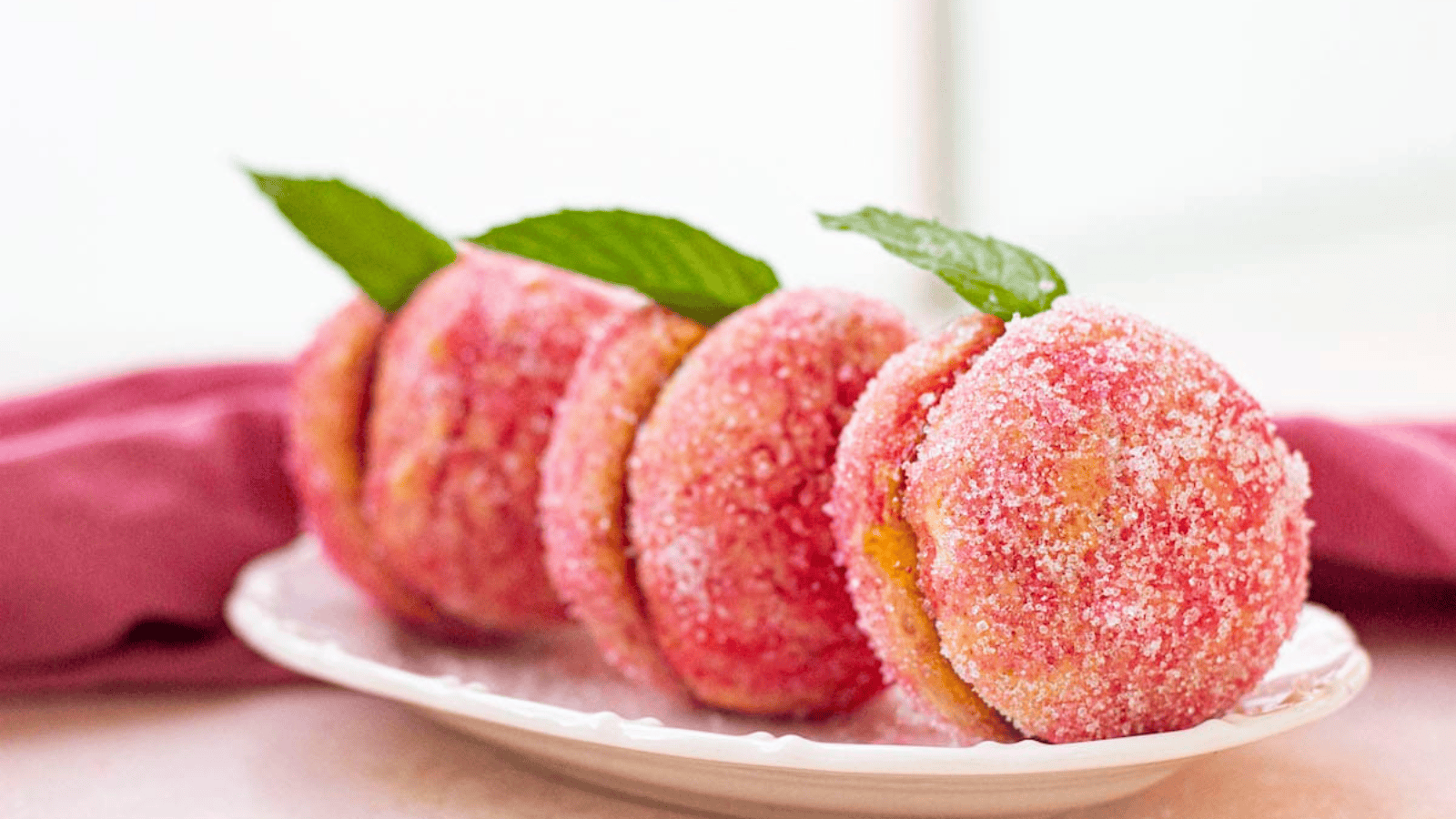 Four sugar-coated peach-shaped cookies with mint leaves on a white plate.
