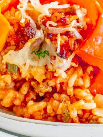 A plate with a stuffed orange bell pepper filled with rice, vegetables, and melted cheese, with a fork beside it.