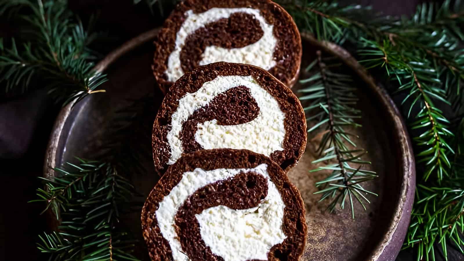Three slices of chocolate and cream Swiss roll on a rustic plate, surrounded by evergreen branches.