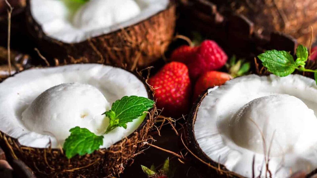 Keto Coconut Ice Cream inside coconut shells with strawberries around.