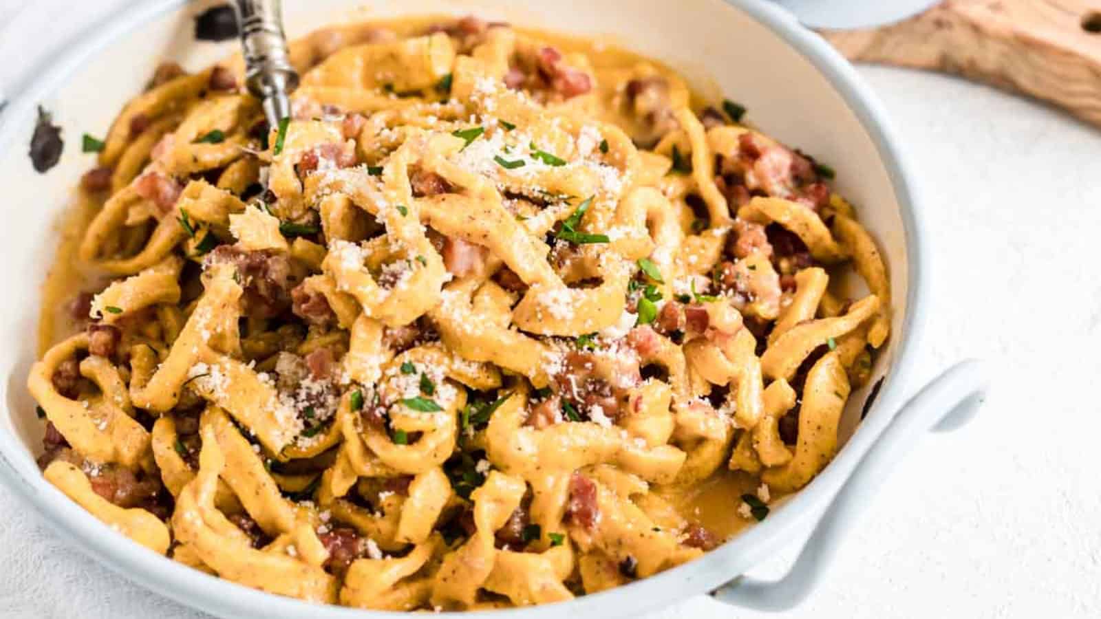 A bowl of creamy pasta with bacon bits, topped with grated cheese and parsley.